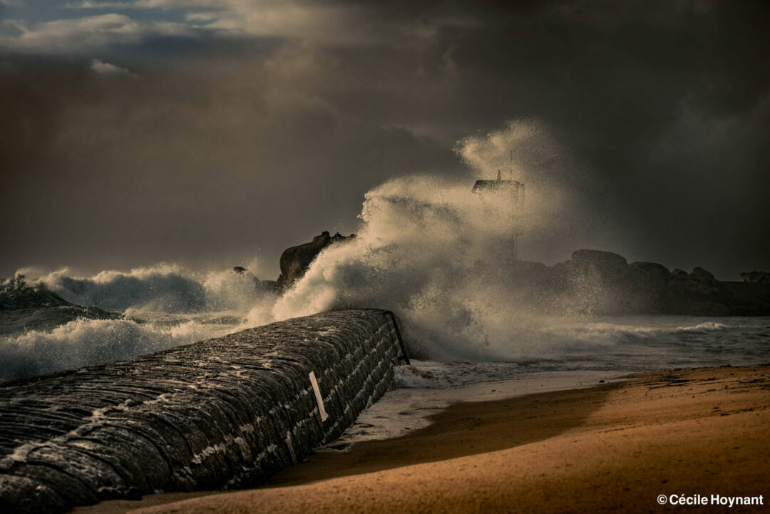 Tempête en Bretagne sur le phare du port de Trévignon. Violentes vagues s'écrasant sur la digue en formant des formes élégantes. Blanc de l'écume contrastant sur un ciel sombre de tempête.