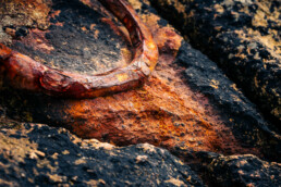 Photographie d'un anneau rouillé servant à amarrer les bateaux. L'anneau a été scellé dans la pierre, une roche de granit sur la place de Rospico en Bretagne dans le Finistère. Le tirage d'art est numéroté et en série limité. Il fait partie de l'exposition Ondes Marines de Cécile Hoynant
