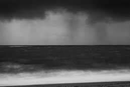 Photo d'art en tirage limité, numéroté et signé, noir et blanc, pose longue, paysage de tempête en Bretagne avec la lumière des phares à l'horizon.