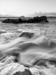 Photographie d'art en noir et blanc, pose longue, mouvement d'écume autour d'une roche pendant une tempête en Bretagne, tirage d'art numéroté et signé en série limitée.