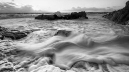 Photographie d'art en noir et blanc, pose longue, mouvement d'écume autour d'une roche pendant une tempête en Bretagne, tirage d'art numéroté et signé en série limitée.