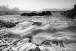 Photographie d'art en noir et blanc, pose longue, mouvement d'écume autour d'une roche pendant une tempête en Bretagne, tirage d'art numéroté et signé en série limitée.