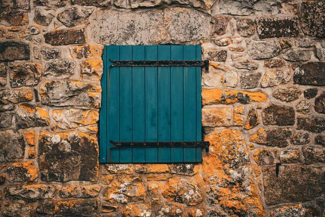 Volet clôt bleu sur une maison en pierres de la presqu'île de Crozon, tapissées de mousse orange.