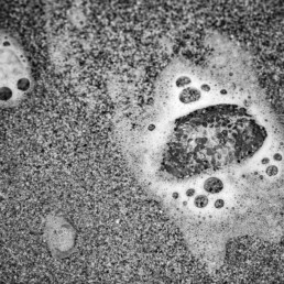 Photographie d'art en noir et blanc d'une méduse faisant un effet loupe sur les grains de sable d'une place bretonne. Tirage d'art numéroté et signé par Cécile Hoynant, photographe de mer en Bretagne. Série limitée. Impression sur papier Fine Art.